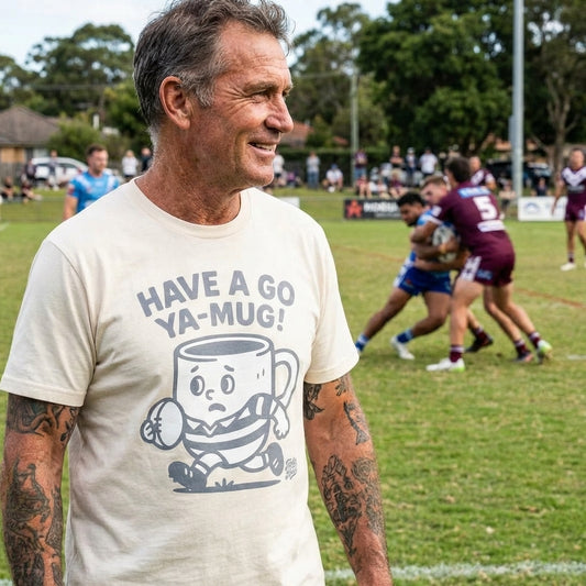 Man wearing a Footy Head t-shirt with a Have a go ya mug graphic on a NRL sports field with players in the background