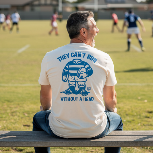 Man sitting on a bench wearing a t-shirt with a graphic and text, watching a NRL game in the background.
