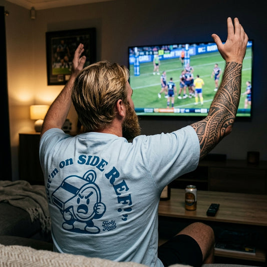 Man watching sports on TV with a Footy Head 'Get'm on side Ref!' t-shirt in a living room.