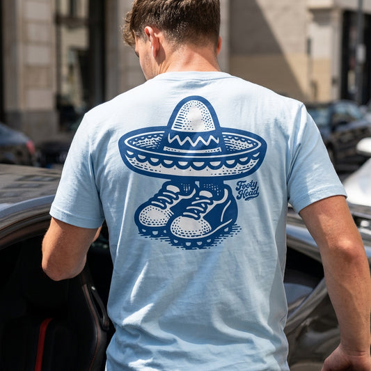 Man wearing a light blue Footy Head Under The Cap t-shirt with a blue graphic on the back, standing next to a car.